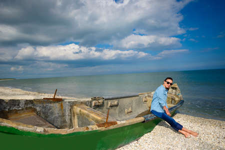 Young woman sitting on an old boat on a beach on a sunny summer dayの写真素材