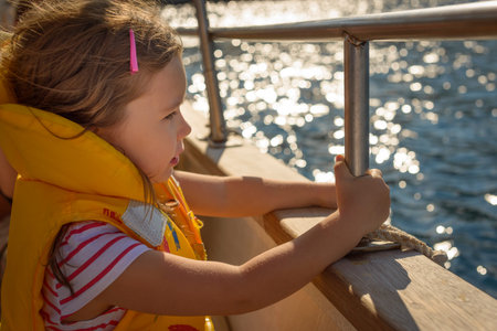 Adorable little girl in a life jacket traveling on boat on beautiful summer dayの写真素材