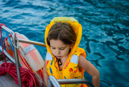 Adorable little girl in a life jacket traveling on boat on beautiful summer dayの写真素材