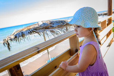 Cute little girl watching aside from the terrace near the sea beach, resting in the shadeの写真素材