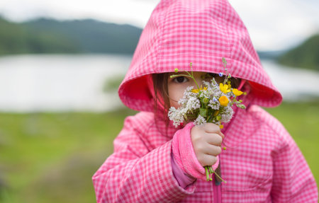 Outdoor portrait of cute little girl on a rainy summer day on the mountain smelling a bouquet of flowersの写真素材