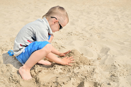 Little boy playing on the beach in the sand. Child sculpts figures out of the sand. Activities in the summer on the sea.の写真素材
