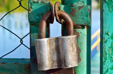 Old padlock hanging on a rusty steel gateの写真素材