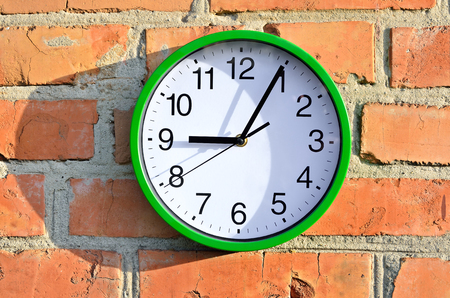 Green wall clock hanging on a brick wallの写真素材