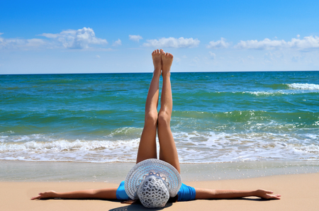 Young girl in a white hat on the sea beach. Clean, sandy beach against the blue sea.の写真素材