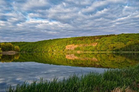 Landscape of a forest lake on a background of cloudy sky.の写真素材