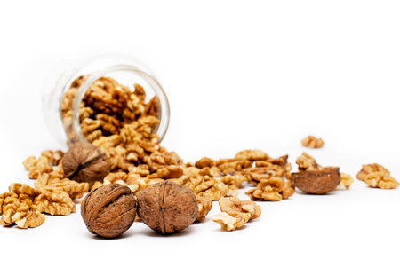 Jar of walnuts with lots of walnuts spilled on the table, on white background.