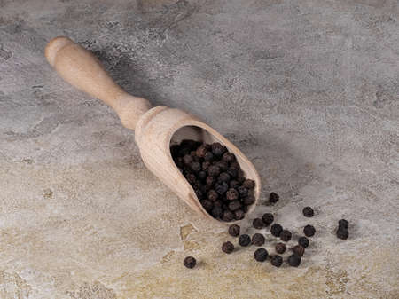 Black peppercorns in wooden shovel for spicesの写真素材
