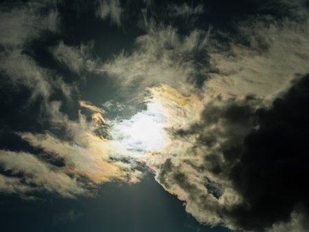 The sun shines through overcast dark yellow-grey storm cloudsの写真素材