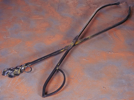 Metal tongs for coals as fireplace accessories on a grunge rusty backgroundの写真素材