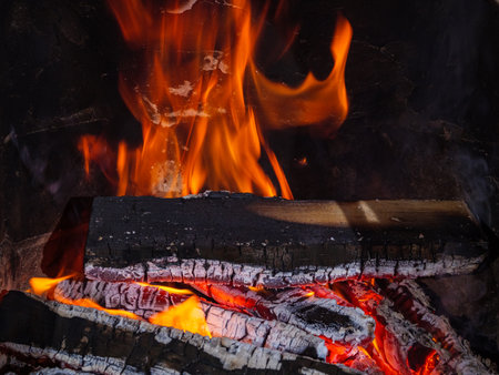 Burning firewood in a fireplace with embers and tongues of flameの写真素材