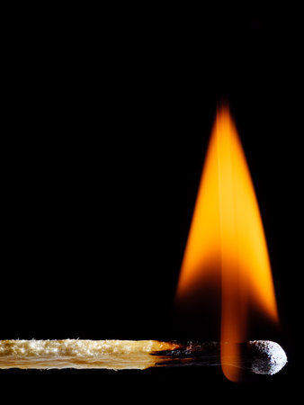 A lit wooden match burns with an orange flame isolated on black backgroundの写真素材