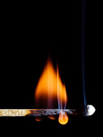 A lit wooden match flaming with an orange flame isolated on black backgroundの写真素材