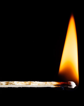 Wooden matchstick flaming with an orange flame against a black backgroundの写真素材