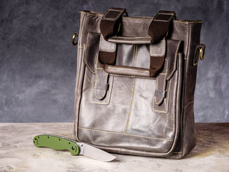 Green folding EDC knife near a leather business casual bagの写真素材