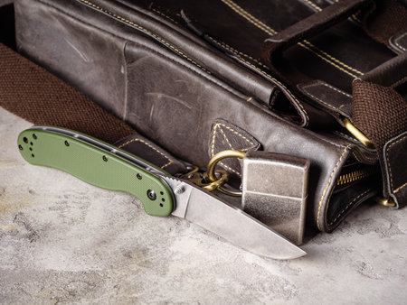 Green folding EDC knife and scratched lighter near a leather casual bagの写真素材