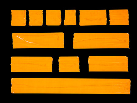 A collection of various torn pieces of orange adhesive tape isolated on a black backgroundの写真素材