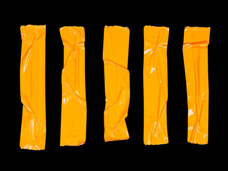 5 crumpled pieces of orange adhesive tape isolated on a black backgroundの写真素材