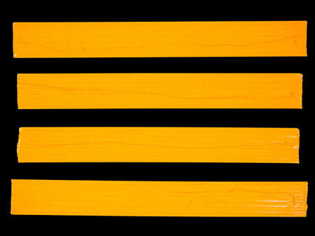 4 horizontal pieces of orange masking tape isolated on a black backgroundの写真素材