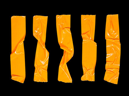 5 crumpled pieces of orange masking tape isolated on a black backgroundの写真素材