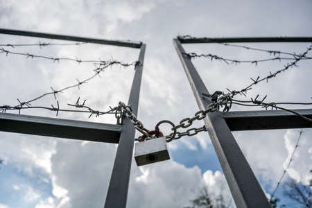 Forbidden area fenced with a barbed wire fence. Gate with padlock closed to the key. Border of States.の写真素材