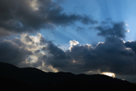 rays of the sun making their way through the clouds against the backdrop of the peaks of the...