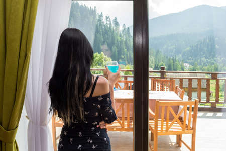 young, beautiful, sexy girl drinking blue champagne enjoying the mountain scenery through a large window.の写真素材