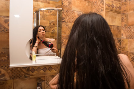 young, beautiful woman dries hair in the bathroom with a hair dryer.の写真素材