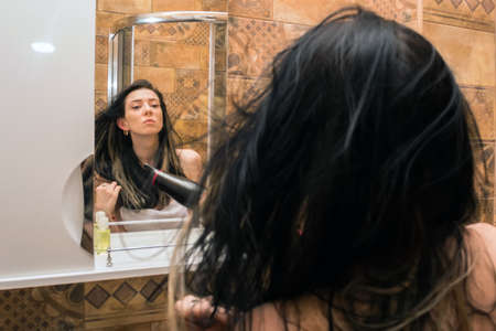 young, beautiful woman dries hair in the bathroom with a hair dryer.の写真素材