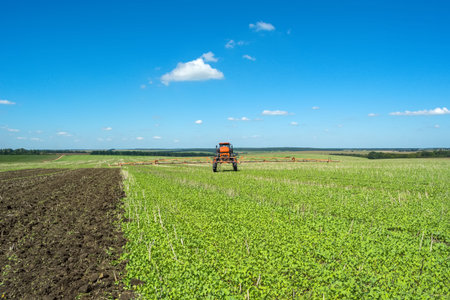 self-propelled sprayer works on a field under a blue sky with clouds.