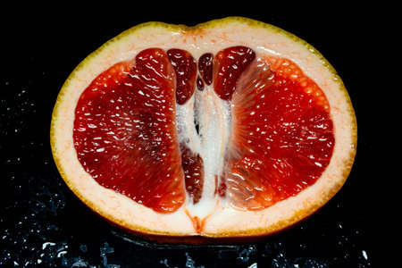 grapefruit pulp with drops of moisture on a black mirror.の写真素材