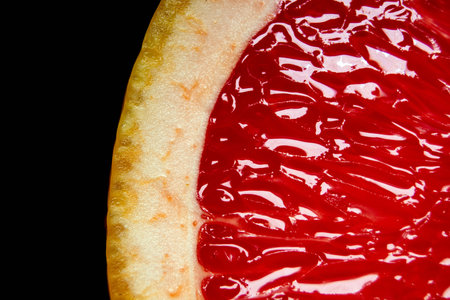 grapefruit pulp with drops of moisture on a black mirror.