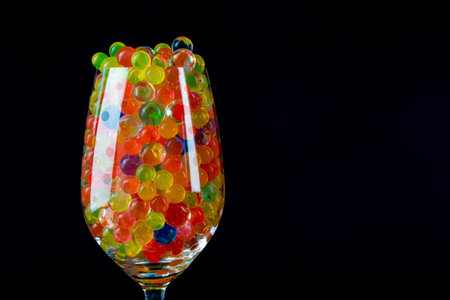 multi-colored silicone gel balls in a glass on a black background.