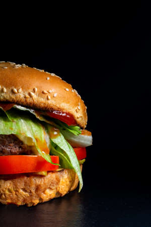 burger with chop, steak, cheese, salad on a black background.の写真素材