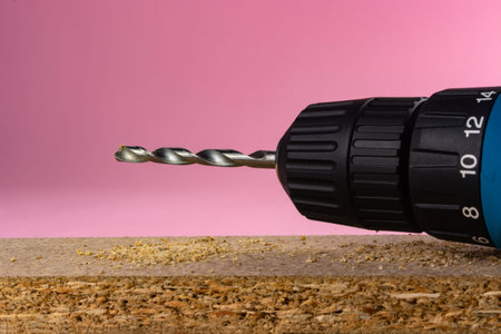 electric drill with a drill on a pink background.