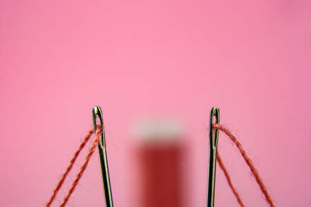 spool with red thread and needle on pink background.の写真素材