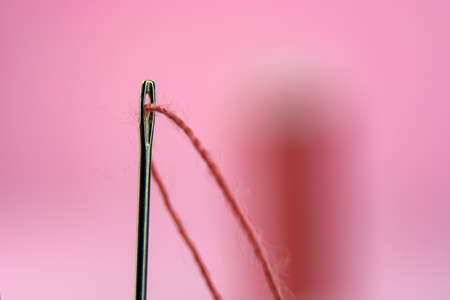 spool with red thread and needle on pink background.の写真素材