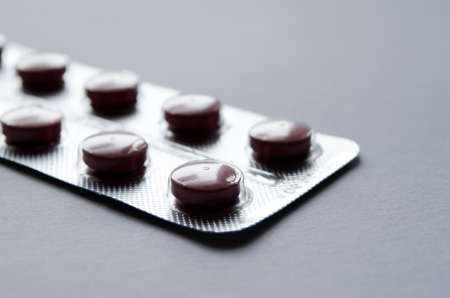 Few dark pills in blister pack close-up on gray background.の写真素材