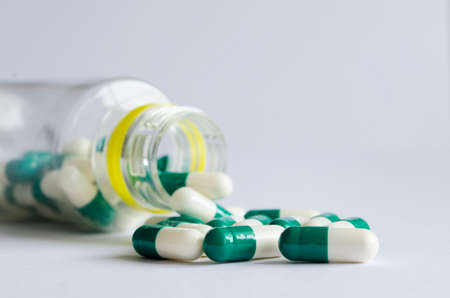 Green and white pills spill out of a plastic jar on light background.の写真素材