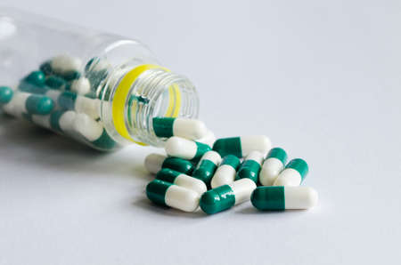 Green and white pills spill out of a plastic jar on light background.の写真素材