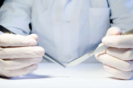 Hands in medical rubber gloves holding metal tweezers and a scalpel.の写真素材