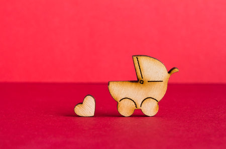 Wooden icon of baby carriage and little heart on red background.