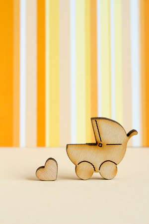 Wooden icon of baby carriage and little heart on orange striped background verticalの写真素材