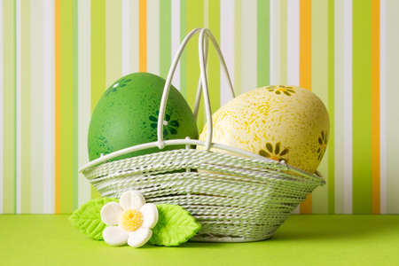 Green and yellow Easter eggs in a basket with white flower.の写真素材