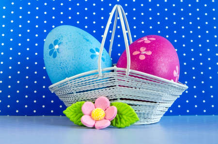 Blue and crimson Easter eggs in a basket with pink flower on blue backgroundの写真素材