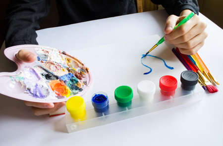 The left hand draws a brush with blue paint on paper in an album with several colorful brushes near it.の写真素材