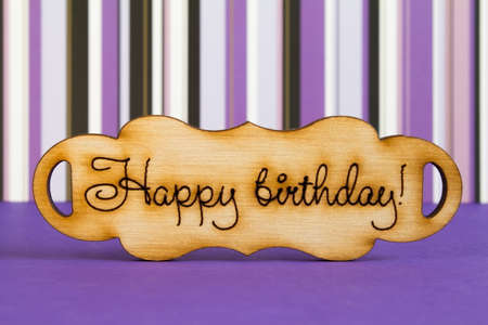 Wooden plaque with the inscription "Happy Birthday" on purple striped background.の写真素材