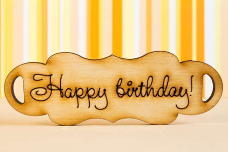 Wooden plaque with the inscription "Happy Birthday" on orange striped background.の写真素材