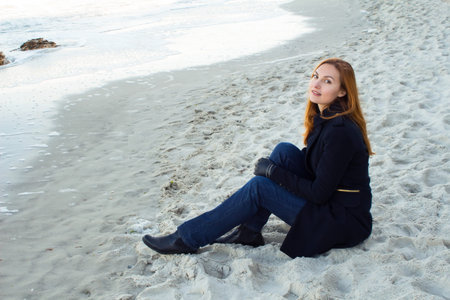Beautiful and style redhead young woman on seaside sitting on sandの写真素材