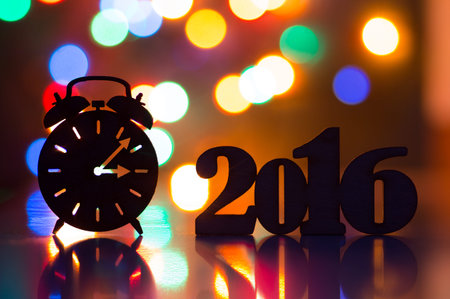 Silhouette of alarm clock and inscription of 2016 year with garland lights on background.